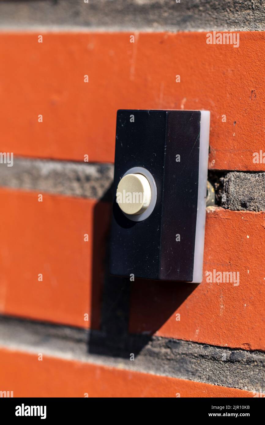 Un retrato de cerca de un viejo timbre negro con un botón blanco en una pared de ladrillo rojo, listo para ser presionado para tocar el timbre y notificar a los residentes. Foto de stock