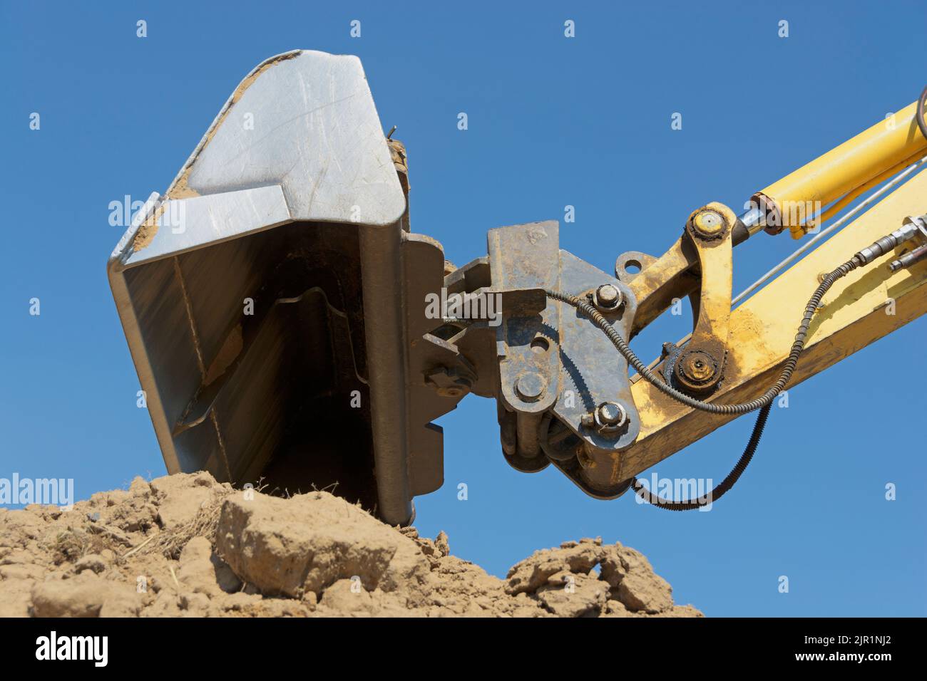 Cubo de excavadora sobre la pila de tierra contra un cielo azul Foto de stock