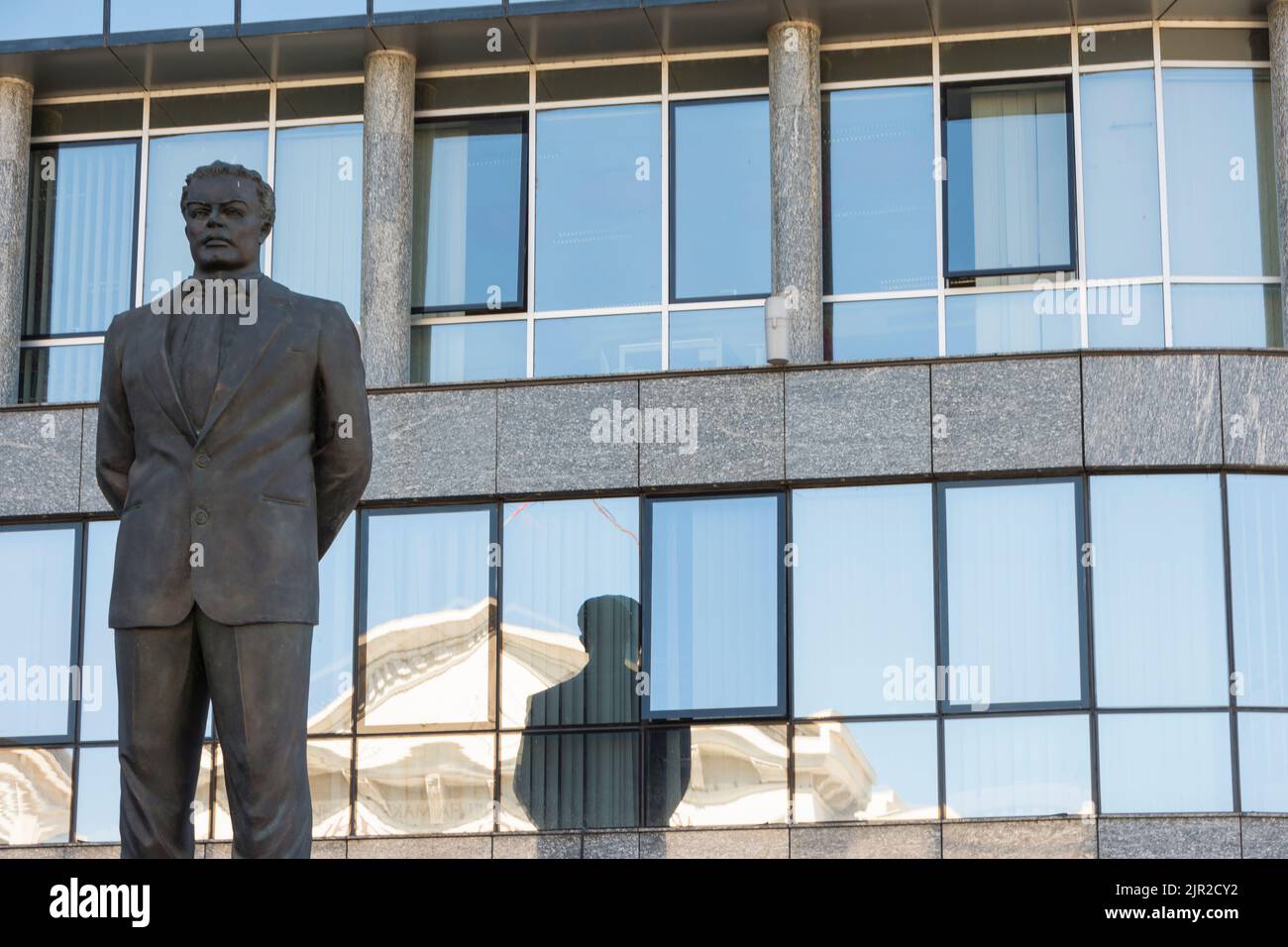 Monumento dedicado al político Nexhat Agolli y su reflejo en las ventanas del edificio Telecom en Skopje, Macedonia del Norte. Foto de stock