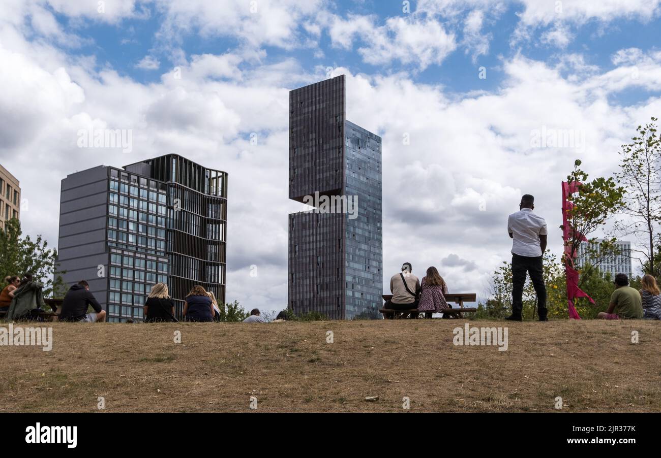 Los lugareños hacen un picnic en E20 Londres durante el verano con los lujosos apartamentos de gran altura de los 'Manhattan Loft Gardens' al fondo, Newham, Londres, 2022. Foto de stock