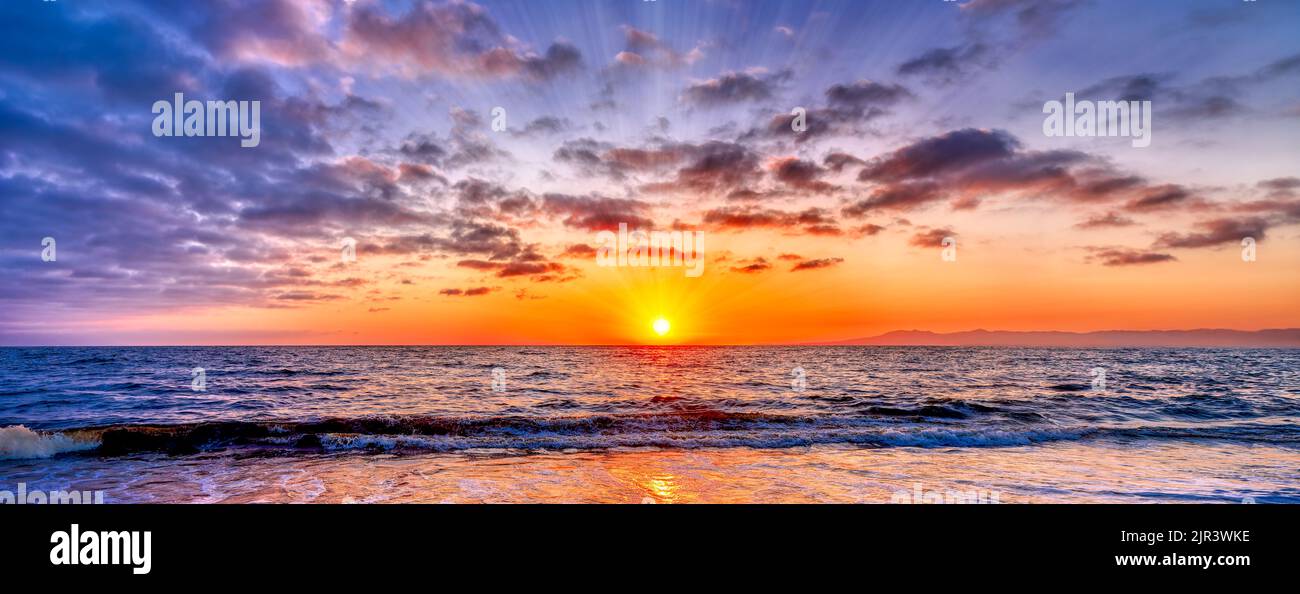 Los rayos del sol están estallando en el horizonte del océano con un cielo vivo y colorido de la puesta de sol en formato de pancarta Foto de stock