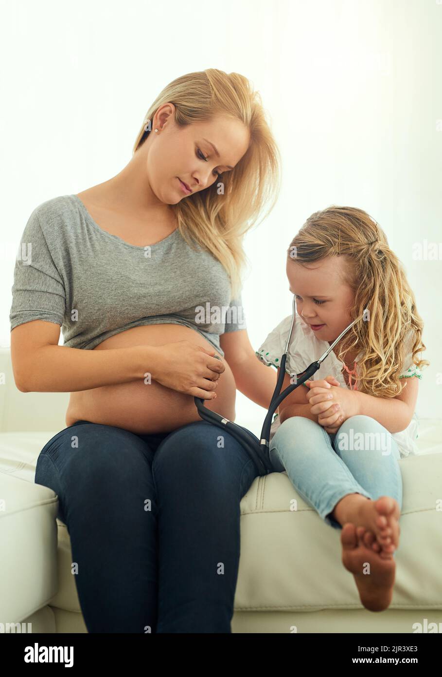 Disfrutar del dulce sonido de bebés ticker. Una niña usando un estetoscopio para escuchar a sus madres embarazadas vientre. Foto de stock