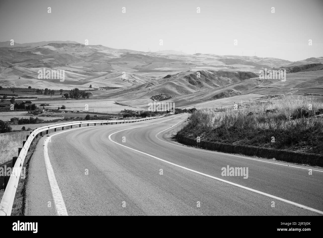 Viaje en blanco y negro por carretera sinuosa en el campo de verano del paisaje occidental de Sicilia, Italia Foto de stock