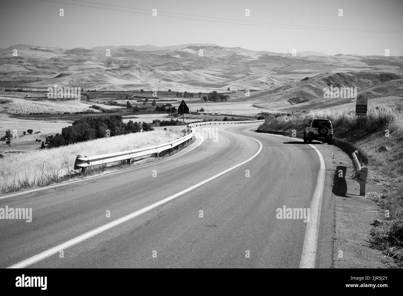 Viaje en blanco y negro por carretera sinuosa en el campo de verano del paisaje occidental de Sicilia, Italia Foto de stock