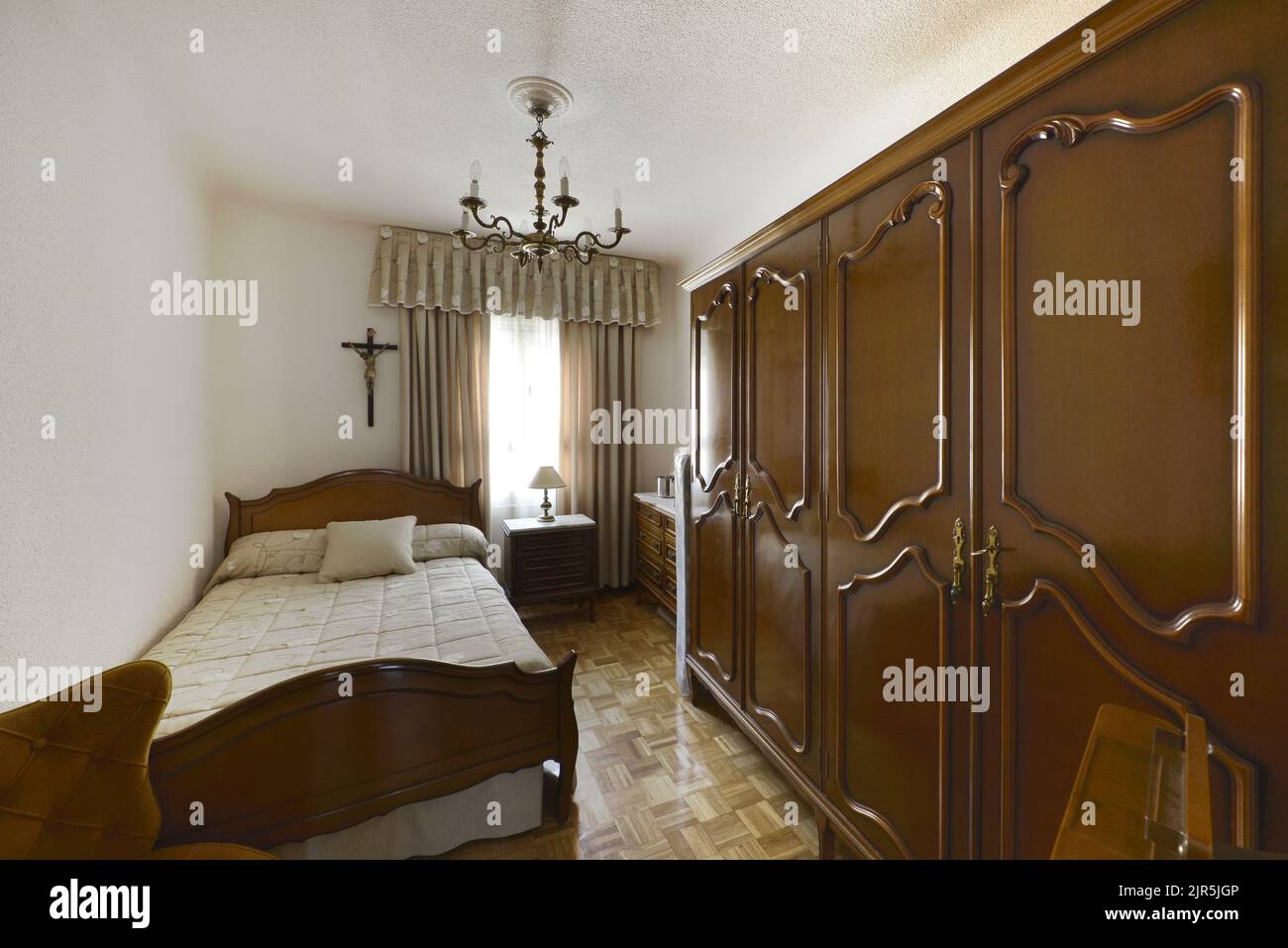 Dormitorio con cama individual, cabecera de madera oscura a juego, armario grande y suelo de parqué de roble claro Foto de stock