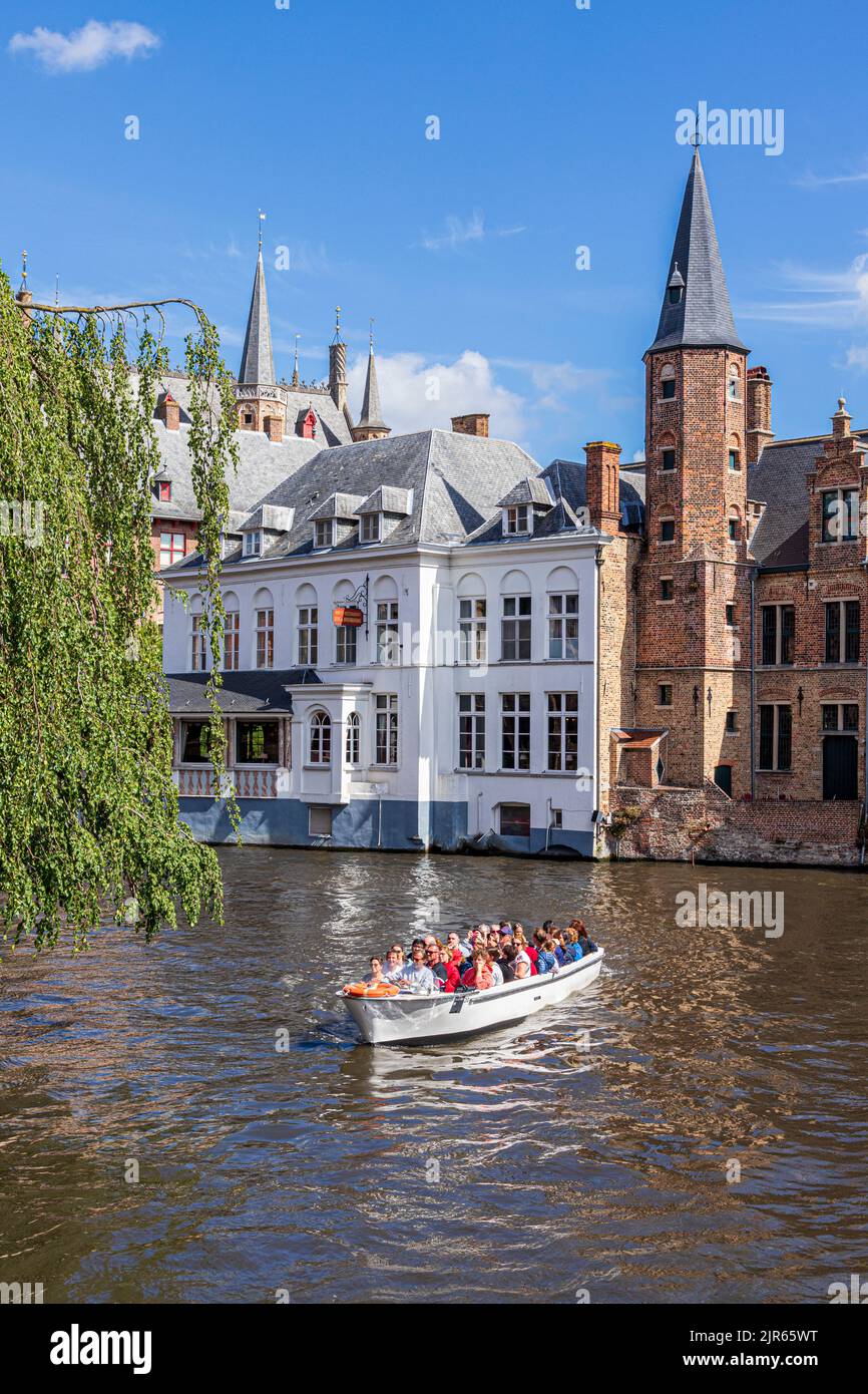 Los turistas disfrutan de una visita guiada en barco por los canales de Brujas, Bélgica. El Duc De Bourgogne Hotel & Restaurant está al fondo. Foto de stock