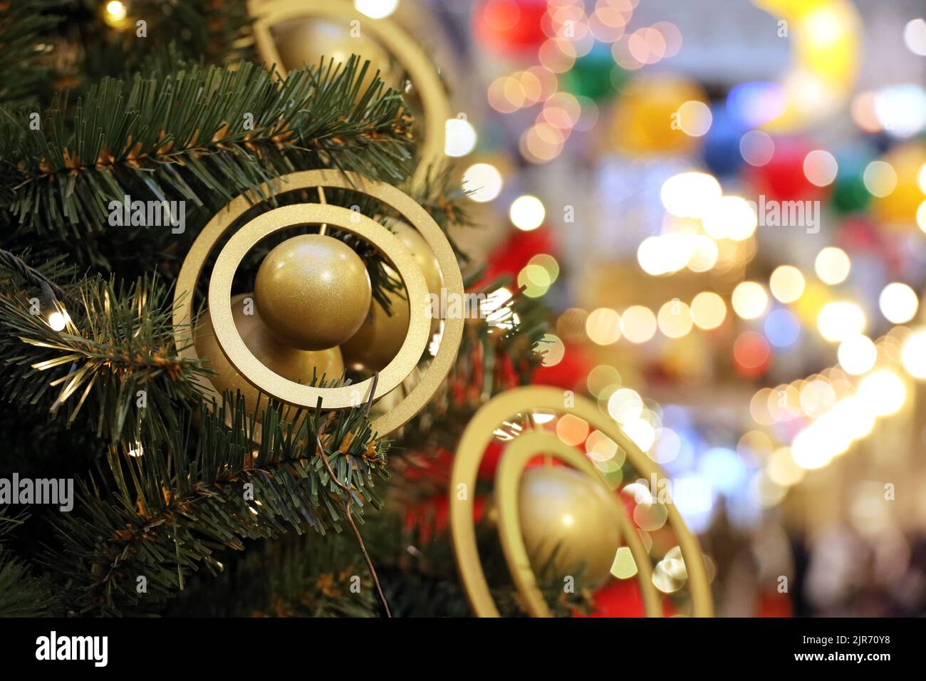 Árbol de Navidad con juguetes dorados en un centro comercial sobre el fondo de luces festivas borrosas. Decoración de Año Nuevo, vacaciones de invierno y rebajas Foto de stock