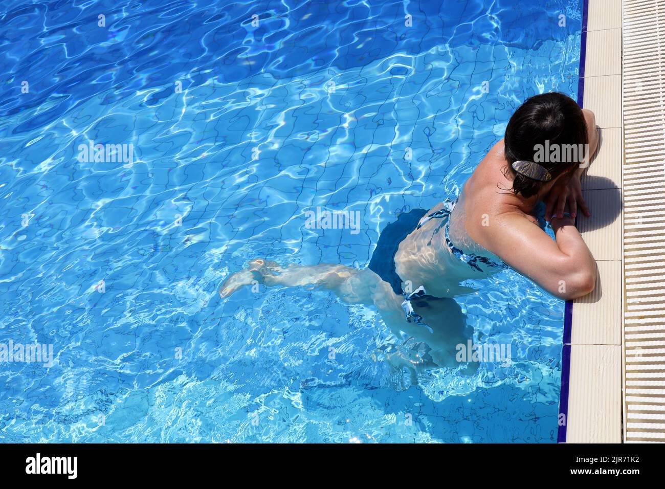 Mujer en traje de baño Relájate en agua transparente apoyándose en el borde de la piscina, vista superior. Chica nadadora en verano, vacaciones de playa Foto de stock
