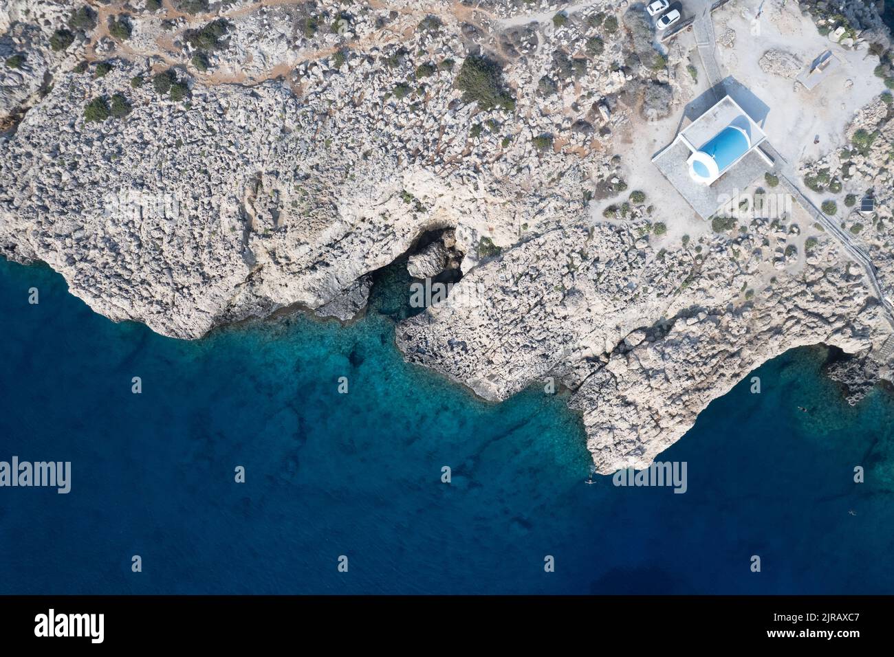 Fotografía aérea de aviones teledirigidos de la península de Cabo Greco con la iglesia Agioi Anargyroi en las rocas. Agua turquesa del océano Foto de stock