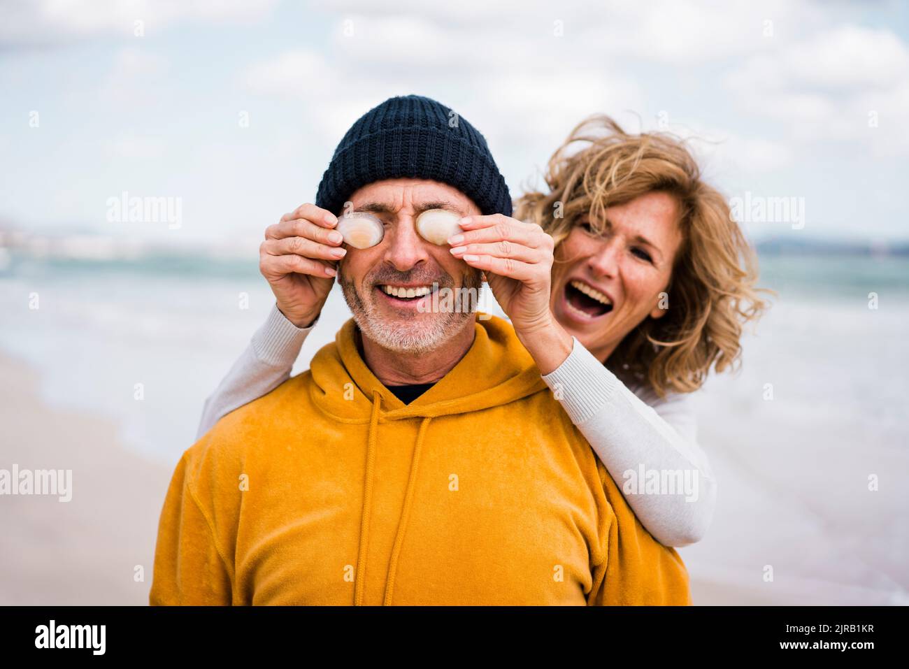 Mujer alegre cubriendo los ojos del hombre con conchas marinas en la playa Foto de stock