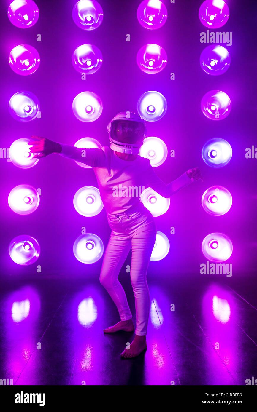 Mujer con casco espacial bailando delante de luces iluminadas púrpura Foto de stock