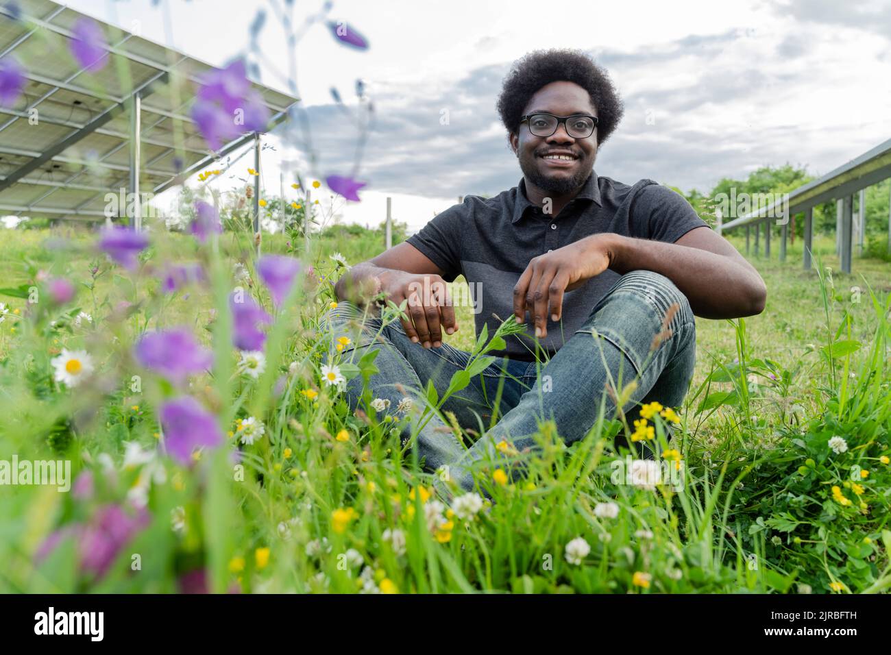 Ingeniero sonriente sentado en la hierba en la central solar Foto de stock