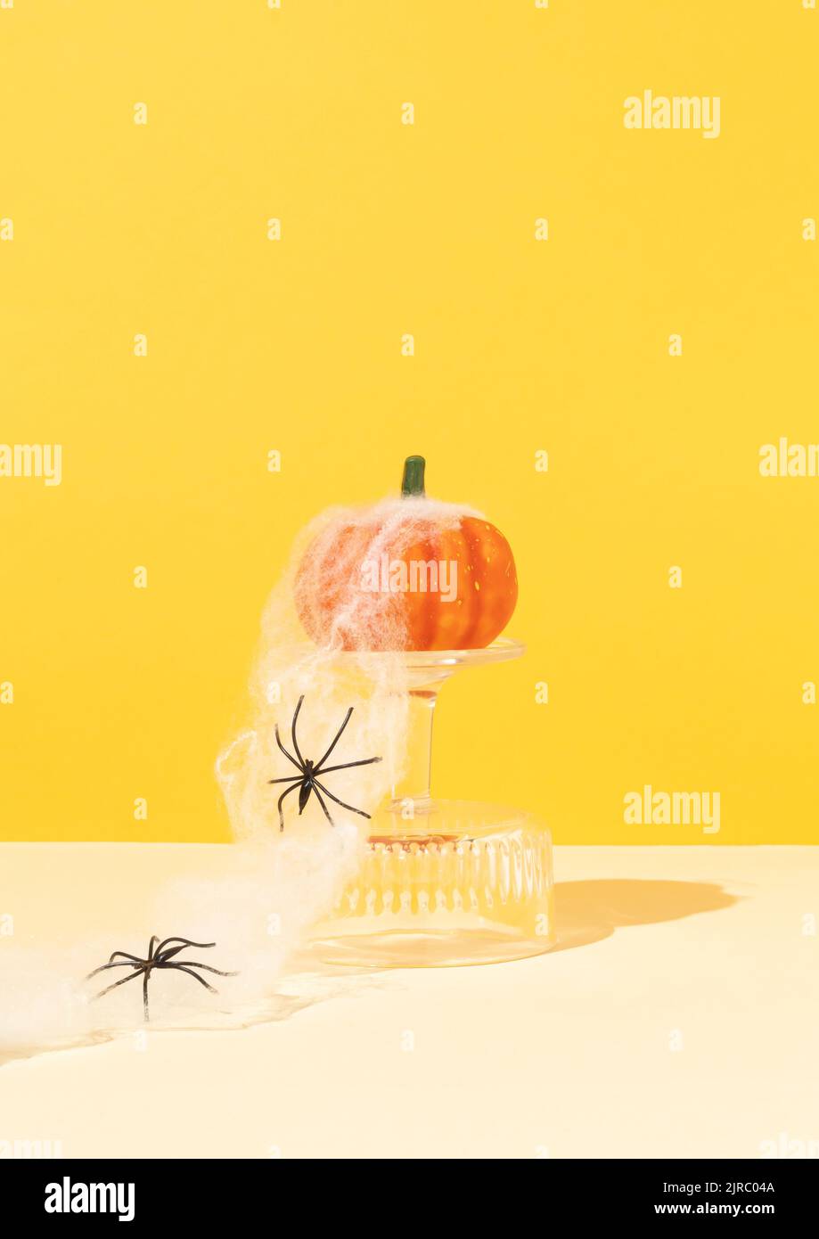Espeluznante composición de Halloween hecha de calabaza en podio de cristal con tela de araña y arañas. Concepto de vacaciones mínimas. Espacio de copia. Foto de stock