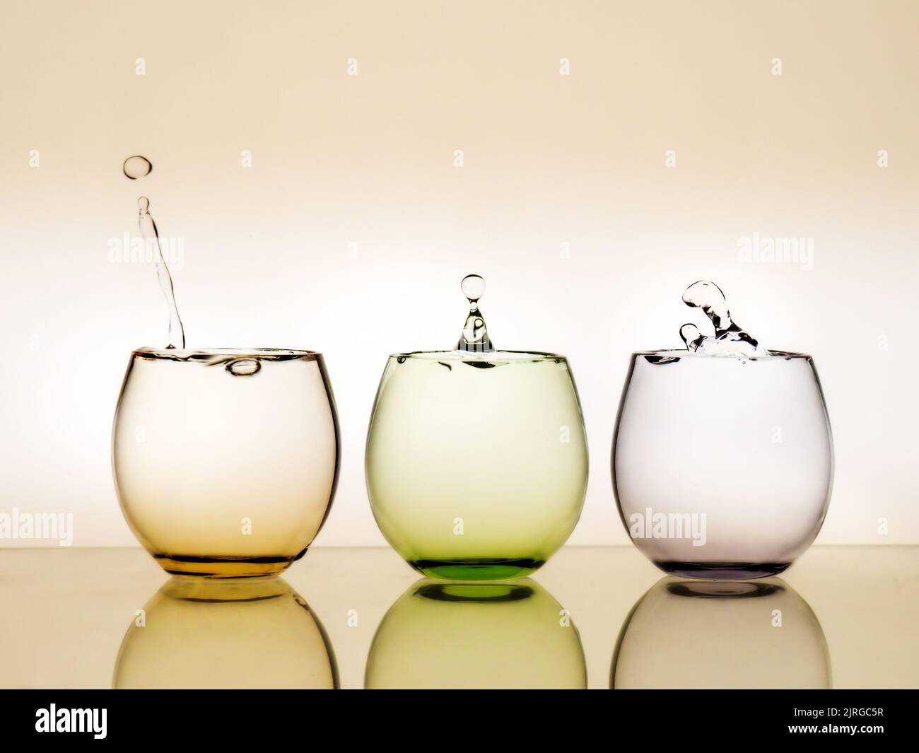 El agua cae. Gotea en tres vasos de colores. Foto de stock