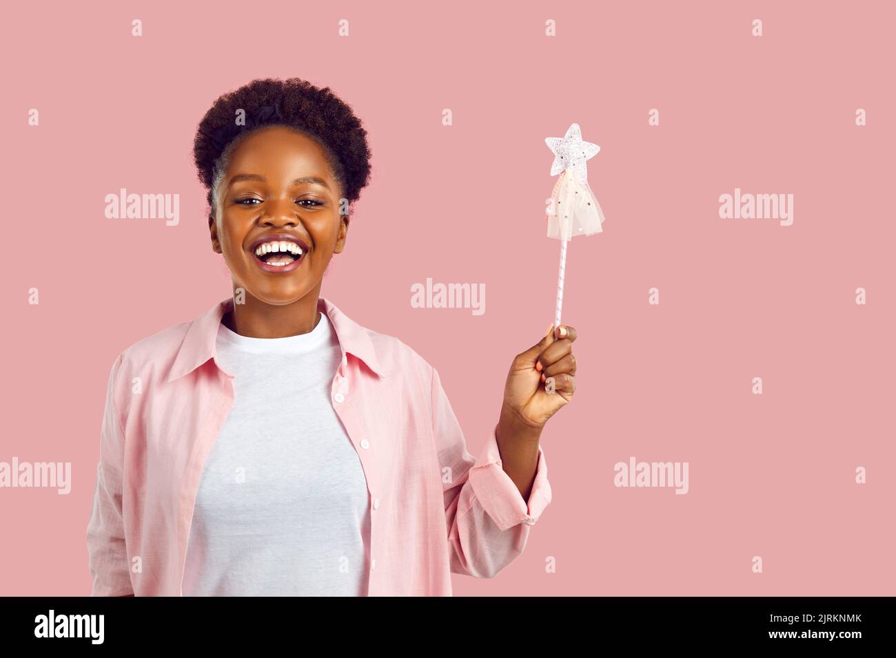 Retrato de feliz divertida mujer joven sonriente con varita mágica sobre fondo de estudio rosa Foto de stock