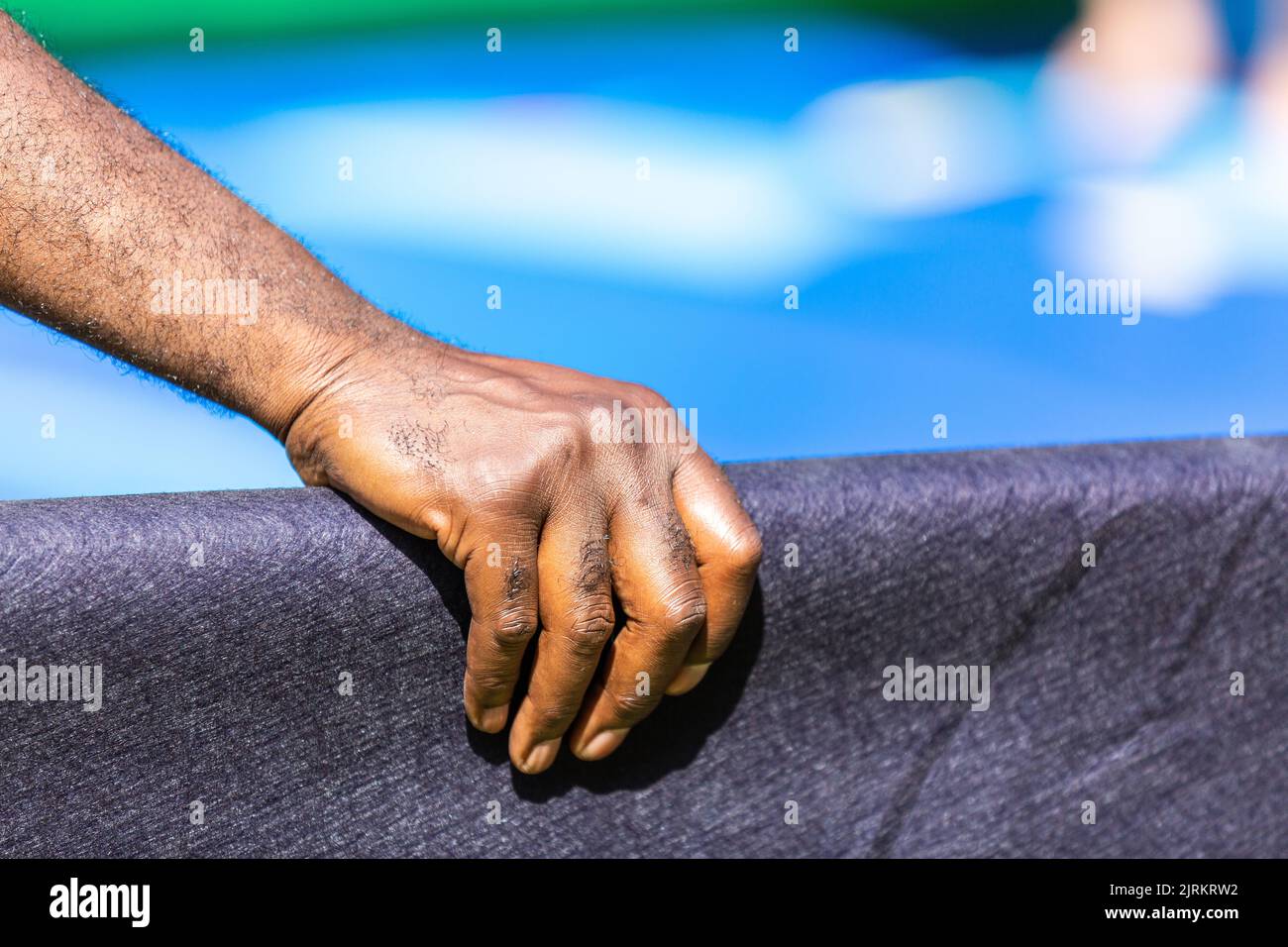 Mano de un hombre de color agarrando una barandilla cubierta de lienzo. Fondo azul. Foto de stock