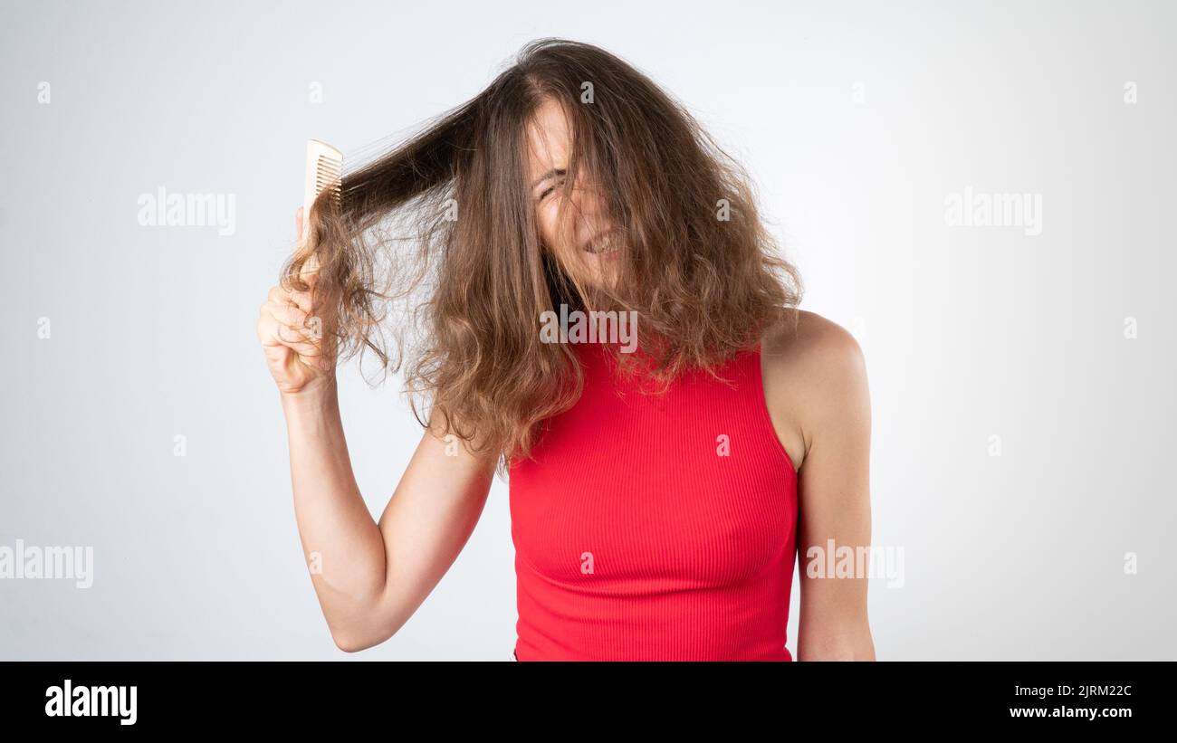 La mueca de una mujer cuando duele, un peinado complejo de pelo enredado rebelde con un peine Foto de stock