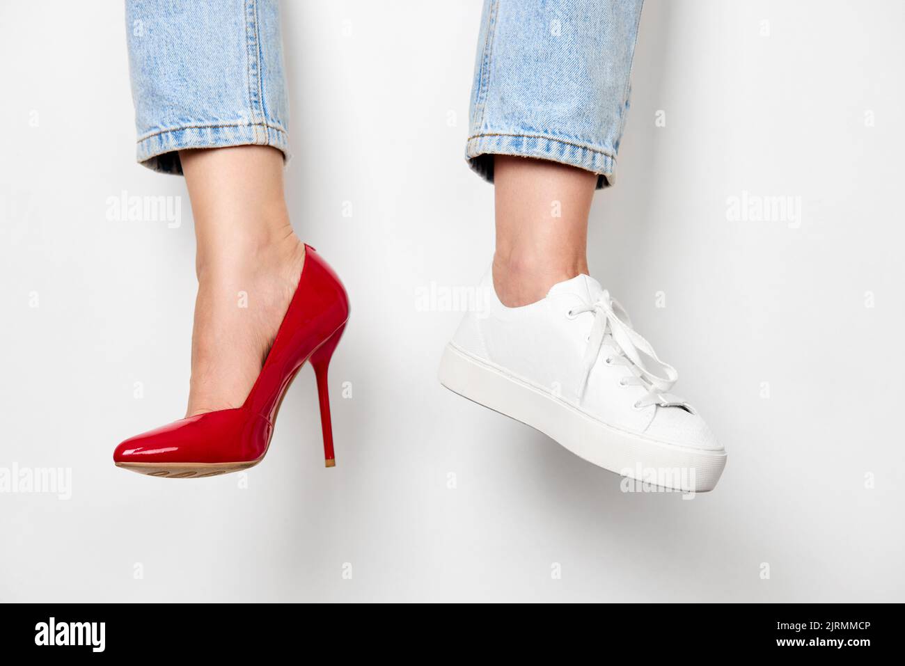 piernas femeninas en zapatillas de deporte blancas y zapatos de tacón alto rojo Foto de stock
