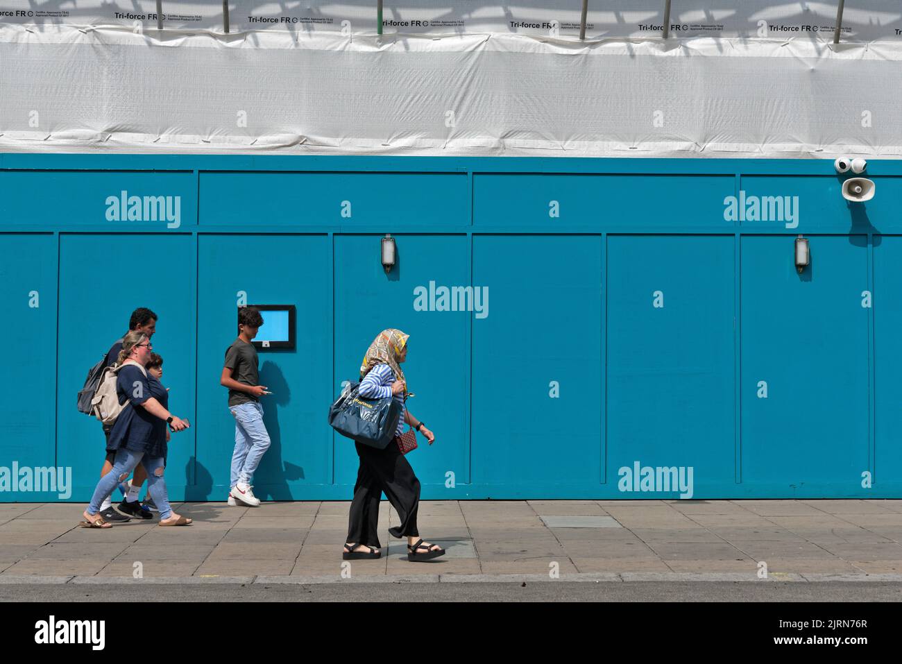 Gente que pasa por un edificio azul acaparando creando una imagen abstracta, en Londres Oxford Street Inglaterra Reino Unido Foto de stock