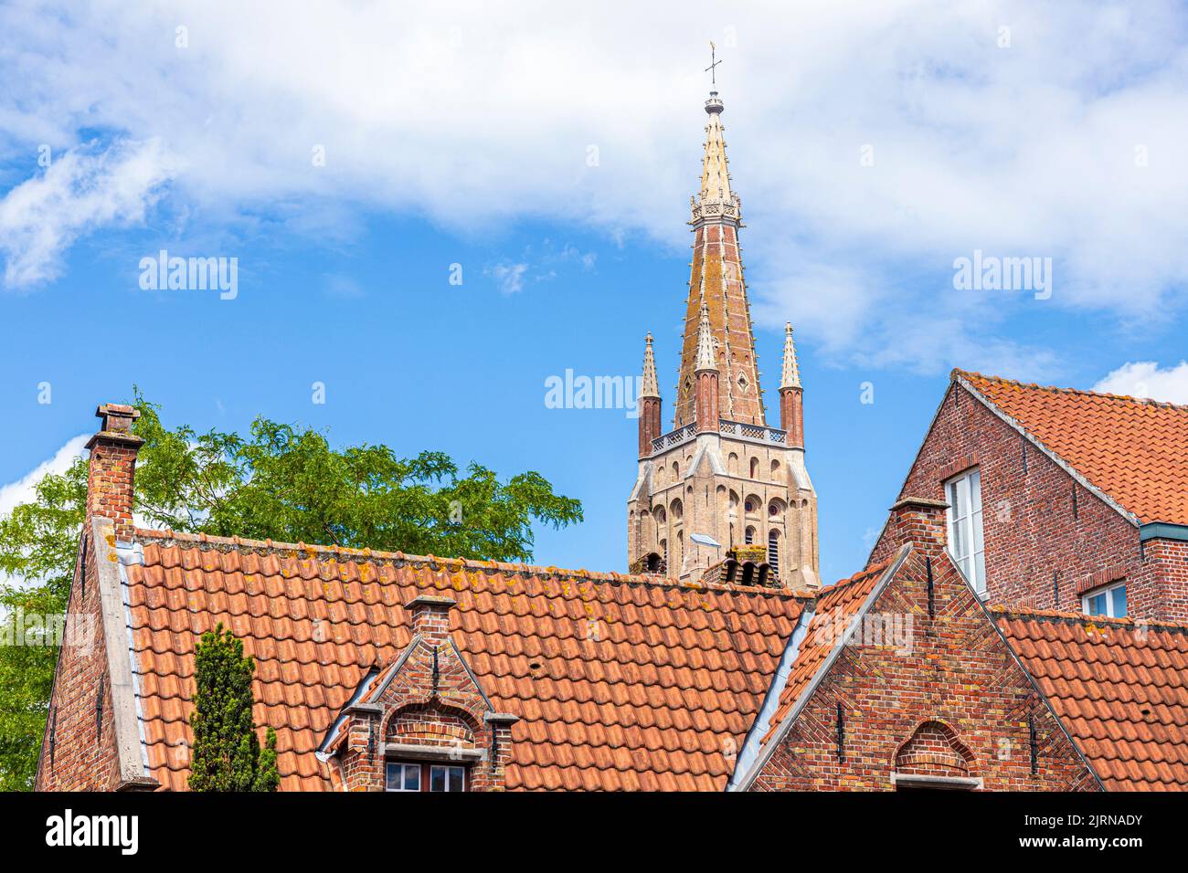 La aguja de la Iglesia de Nuestra Señora (Onze-Lieve-Vrouwekerk) con vistas a los techos pantanados de casas antiguas en Brujas, Bélgica Foto de stock