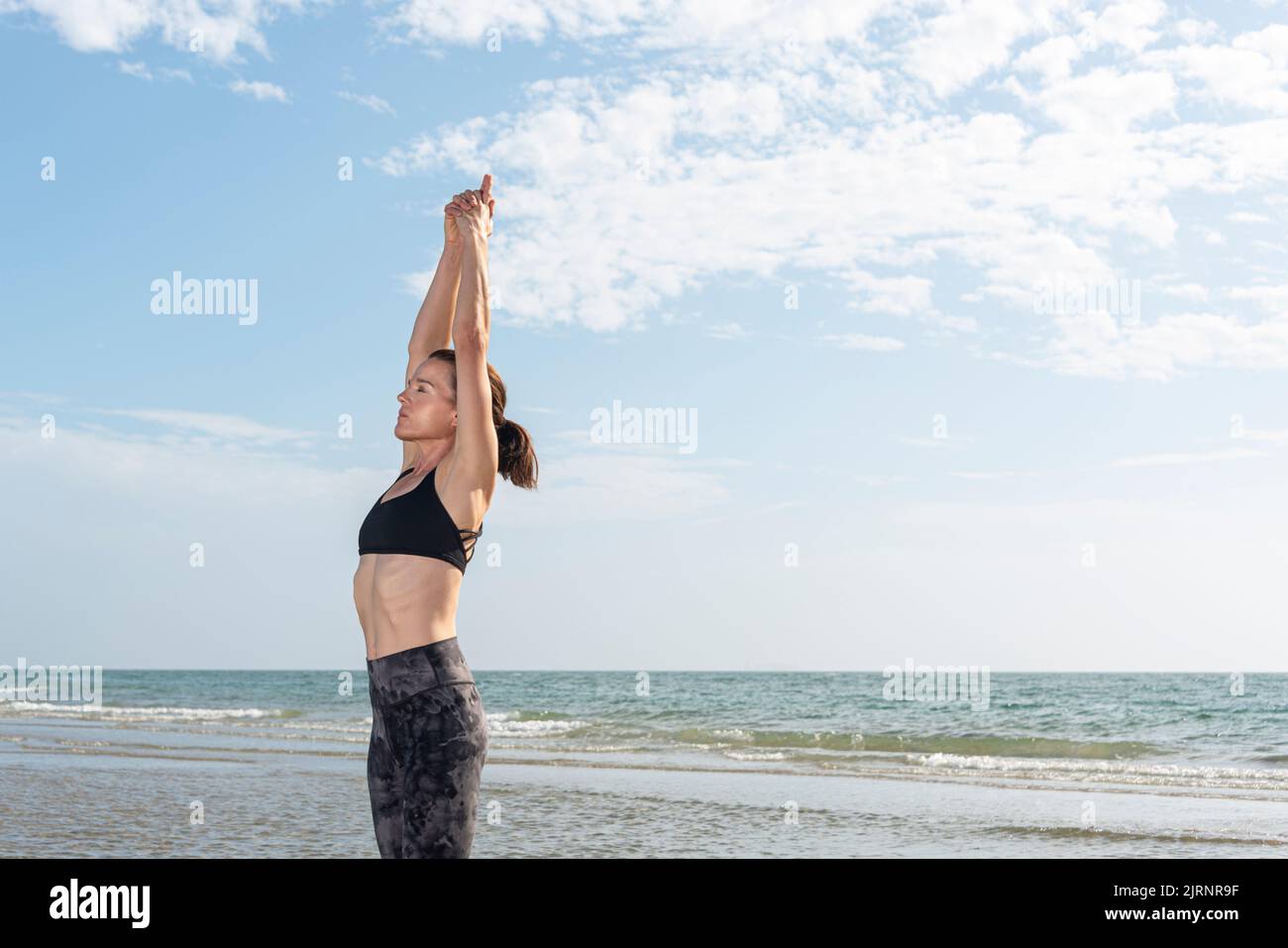 Mujer deportiva en forma practicando yoga junto al mar Foto de stock