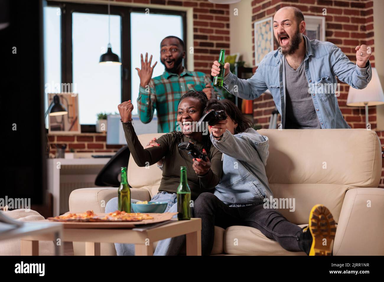 Diversos grupos de amigos que celebran los videojuegos ganan juntos, jugando a la competencia en la fiesta con alcohol. La gente se siente feliz por la victoria y ganar, bebiendo cerveza en casa. Foto de stock