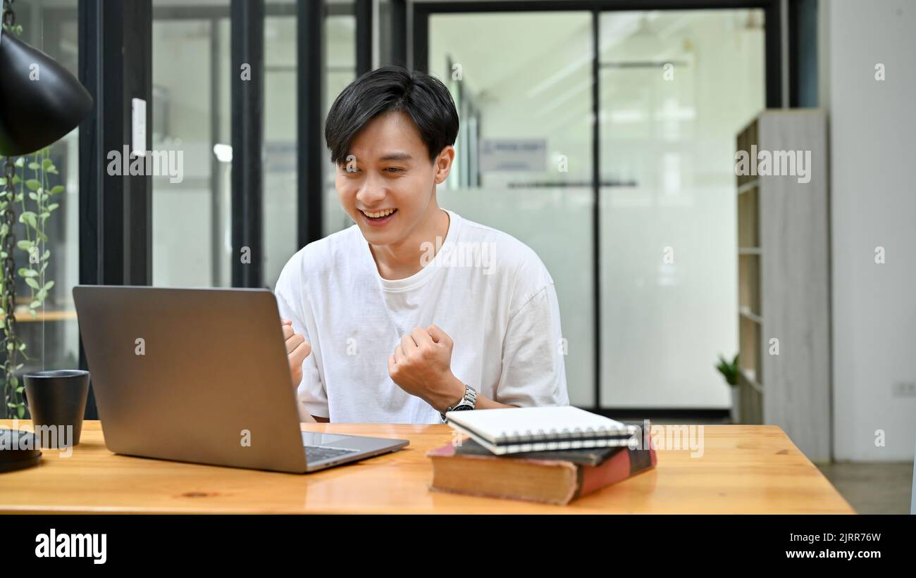 Un joven asiático se siente feliz después de obtener un maravilloso correo electrónico, promoción de empleo, pasar el examen, ganar la lotería, o el éxito del proyecto. Foto de stock