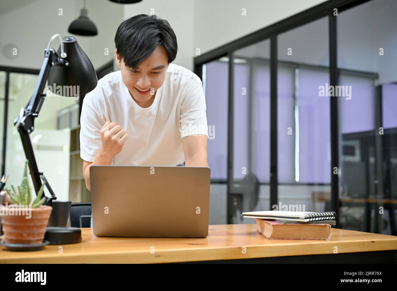 Hermoso joven asiático mirando la pantalla de la computadora portátil, sintiéndose feliz después de obtener un maravilloso correo electrónico, promoción de trabajo, pasando el examen, ganando la lotería Foto de stock