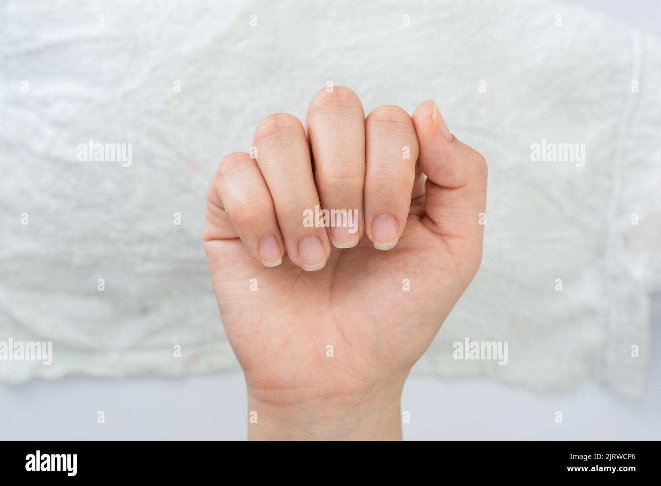 mano de una mujer latina mostrando sus uñas en una posición cerrada de la mano, en el fondo una toalla blanca, uñas semi arregladas listas para la pintura y decoración de uñas Foto de stock