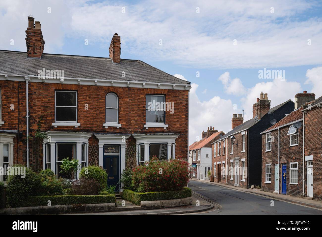 Casas adosadas, una con jardín frontal en flor, en la calle St John y Minster Moorgate todo bajo el cielo azul en Beverley, Reino Unido. Foto de stock