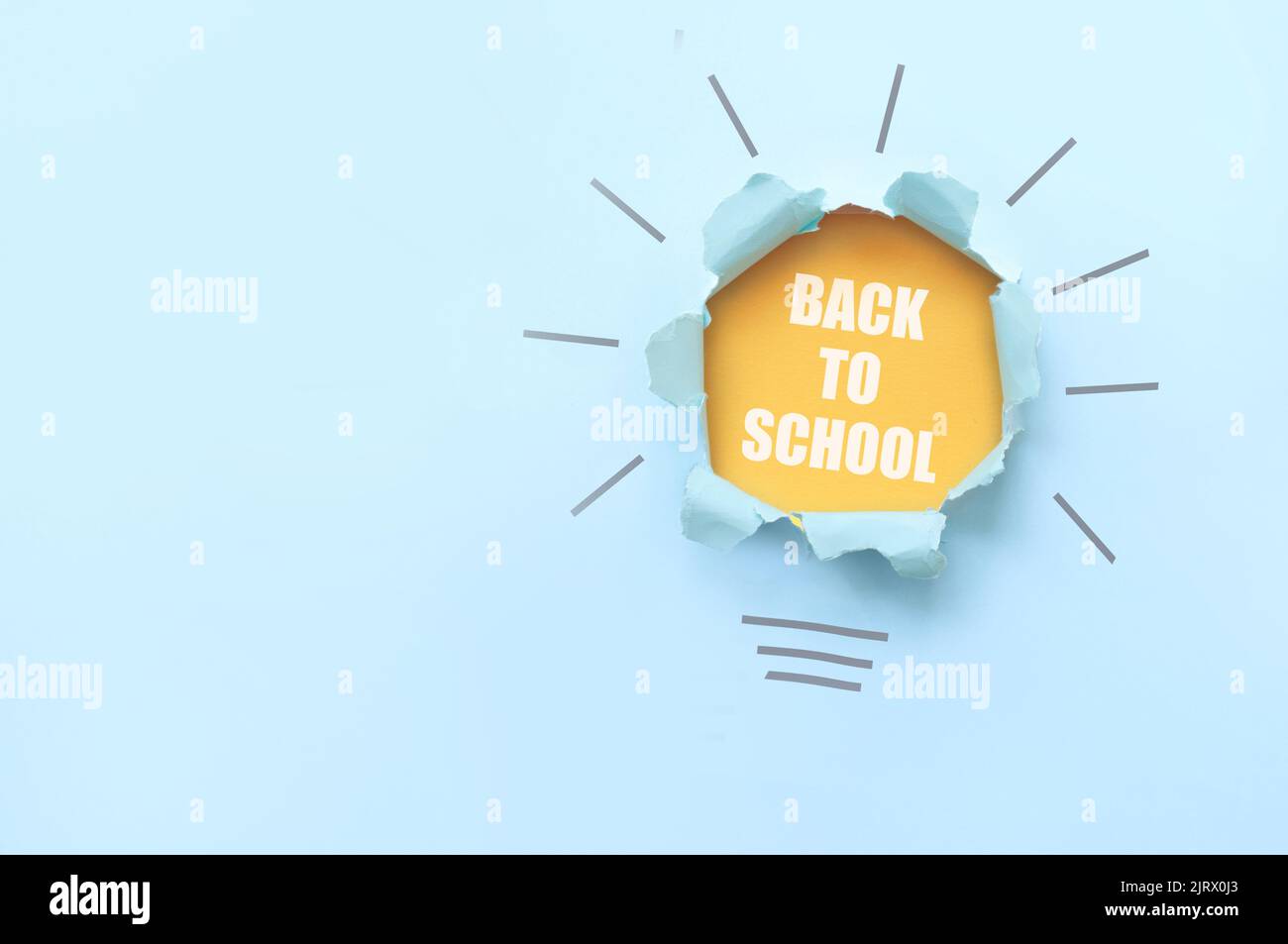 La forma de la bombilla de vuelta a la escuela se revela a partir de un papel rasgado con una capa naranja debajo Foto de stock