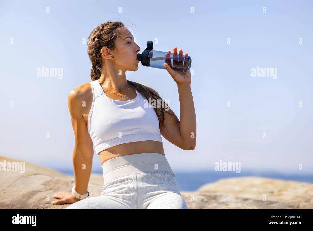 Mujer Atleta Agua Potable durante el entrenamiento al aire libre junto al mar Foto de stock