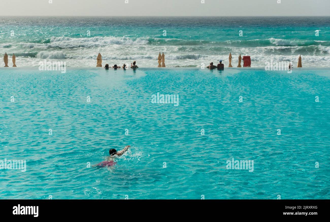 Gente en una piscina con borde infinito frente al océano Foto de stock