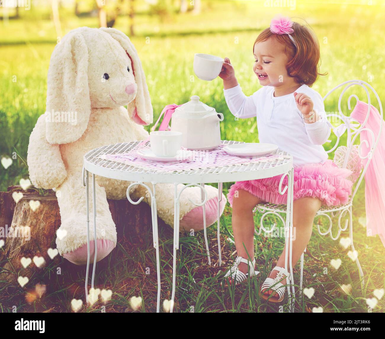 No hay límites a su imaginación. Una pequeña chica linda que tiene una fiesta de té con su animal de peluche en el césped afuera. Foto de stock