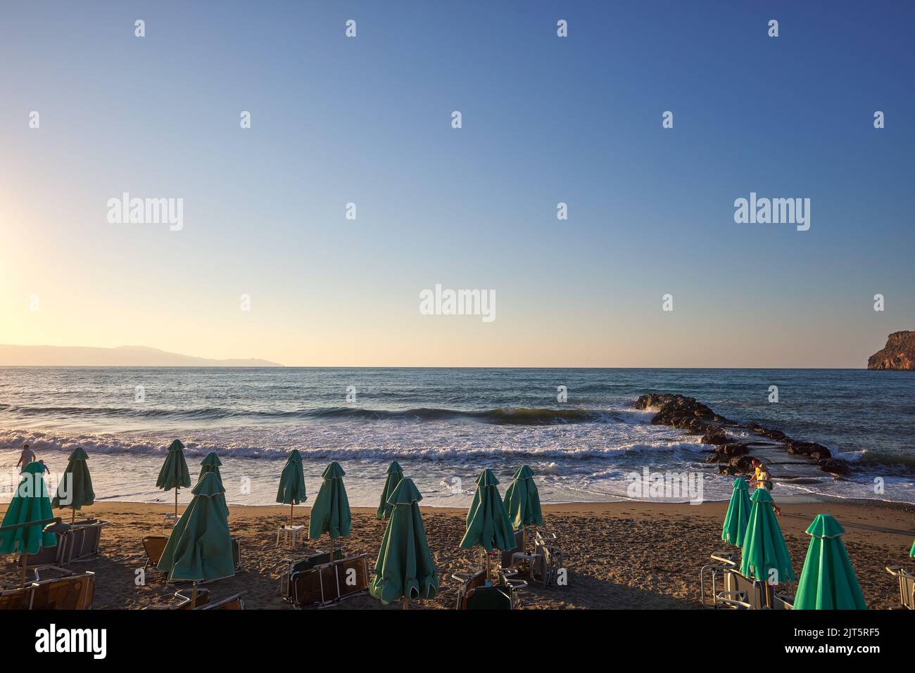 Tumbonas y sombrillas vacías en la playa al atardecer en Chania Creta - Grecia Foto de stock