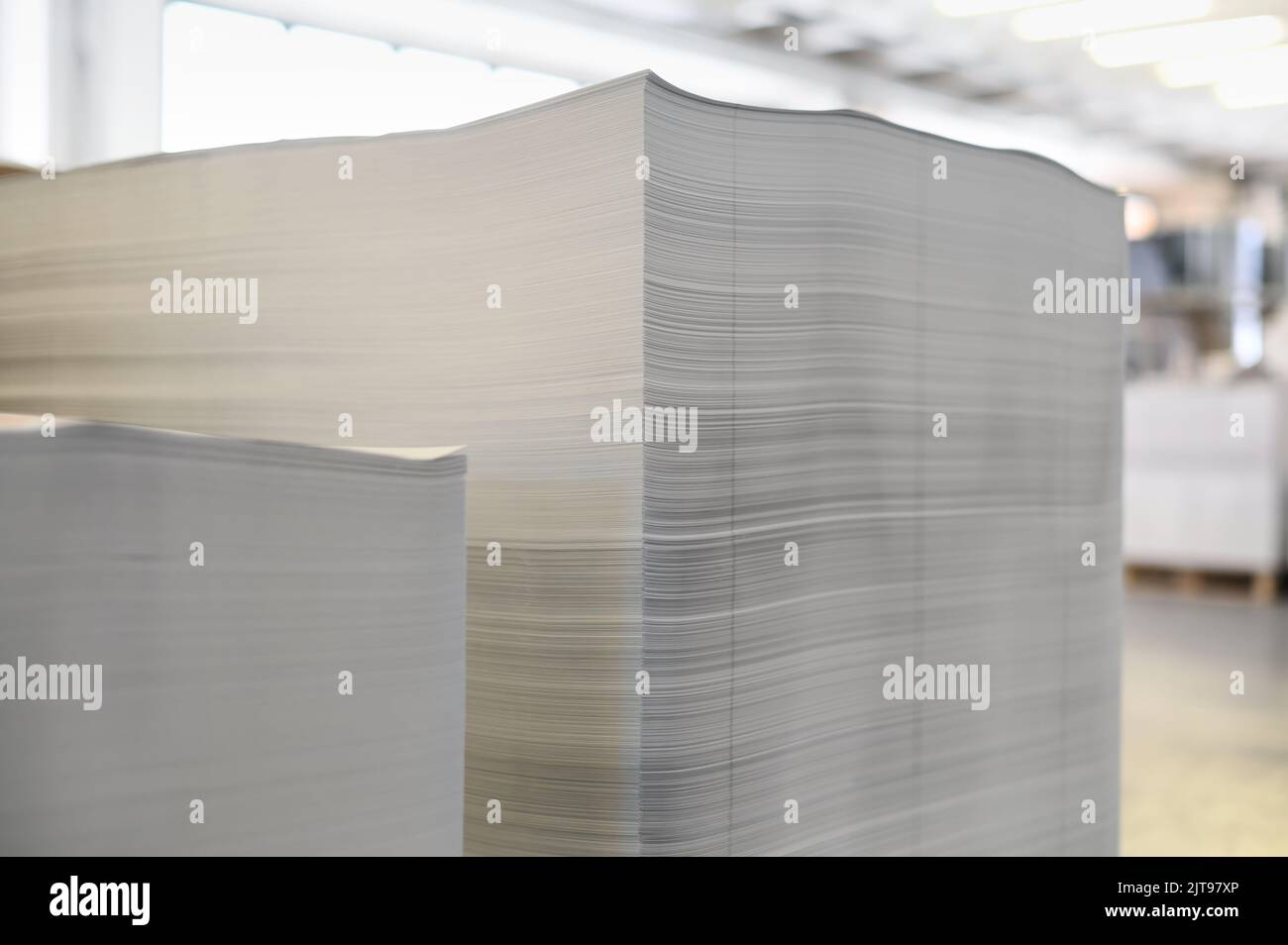 Hojas de papel de impresión blancas apiladas durante la jornada laboral en un taller de tipografía profesional iluminado por el sol Foto de stock