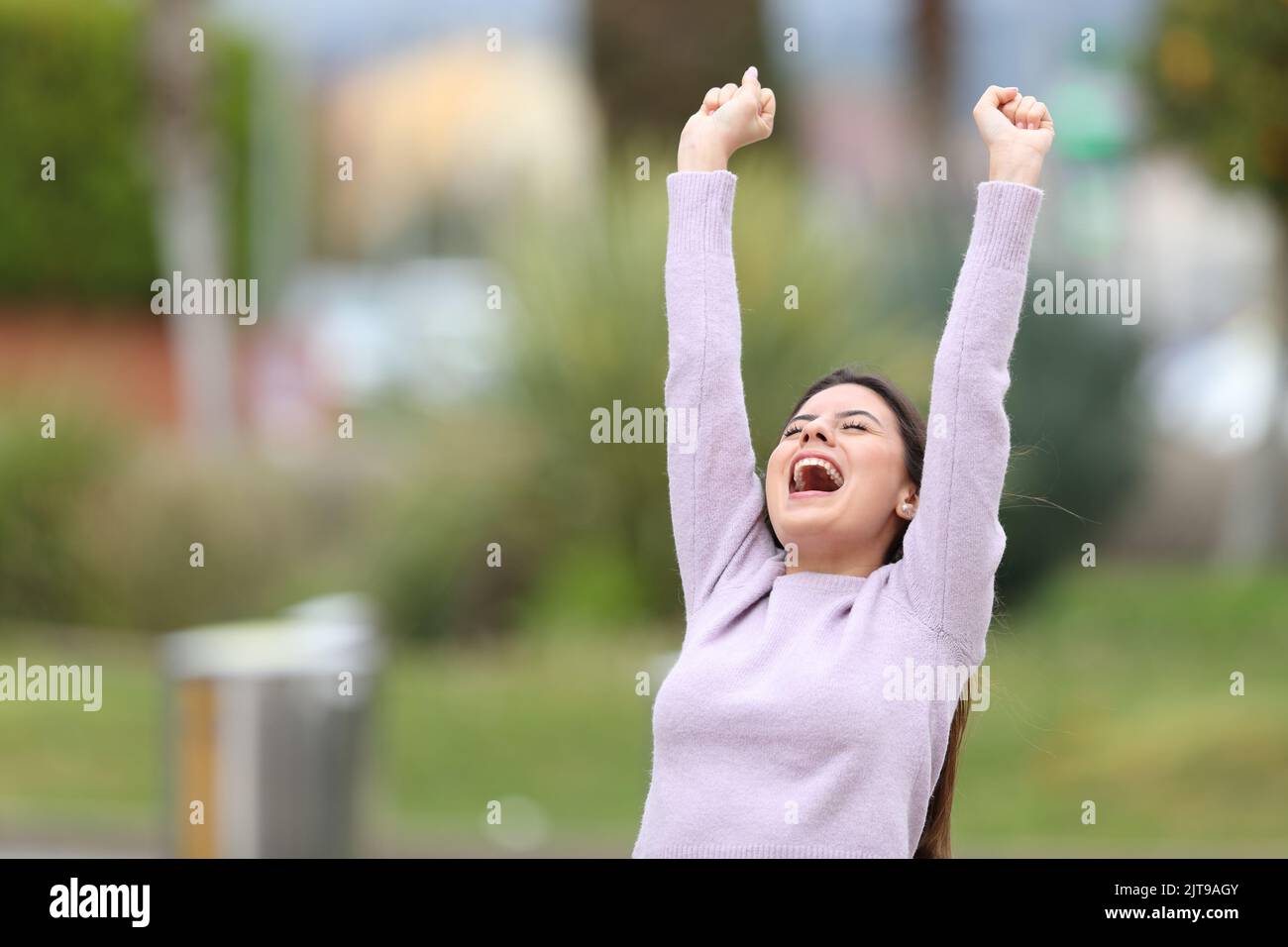 Emocionado adolescente levantando brazos celebrando el éxito en un parque Foto de stock