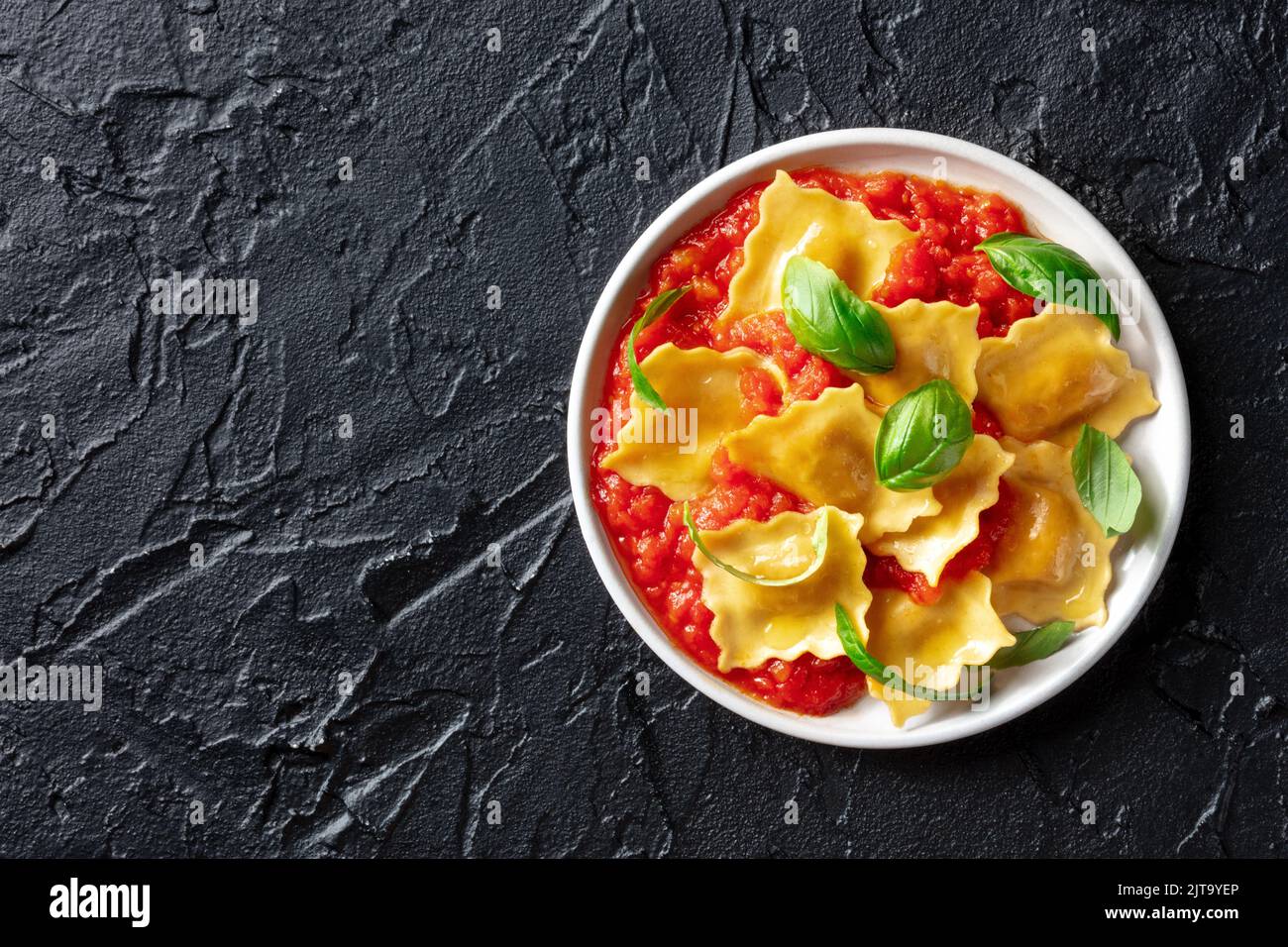 Un plato de ravioli con salsa de tomate y albahaca, comida italiana sencilla, tomada desde arriba sobre un fondo negro con un lugar para el texto Foto de stock