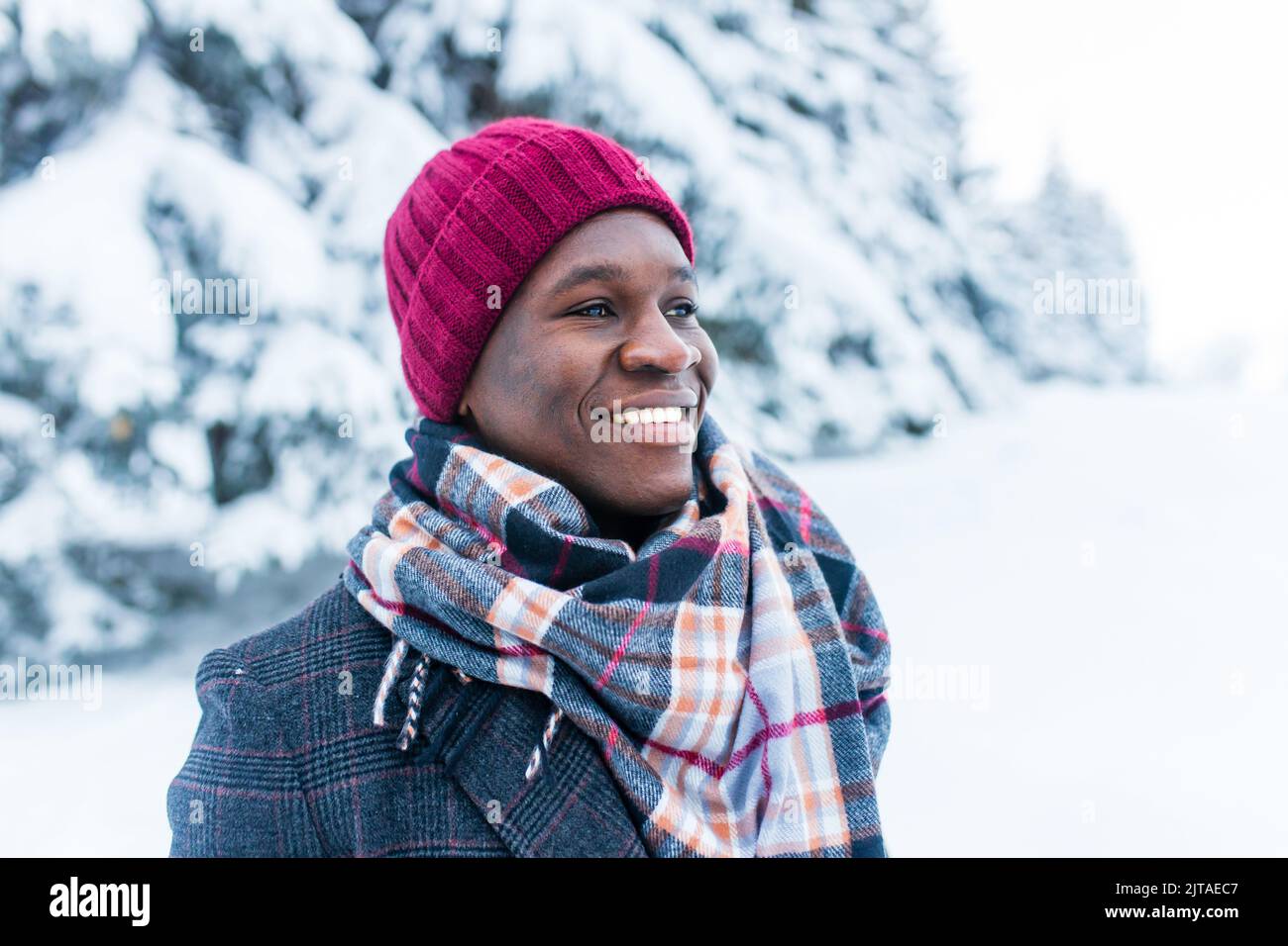 hombre de mano afroamericano con sombrero rojo y elegante abrigo a cuadros mirar la cámara con una sonrisa blanca de nieve enana al aire libre en el parque Foto de stock