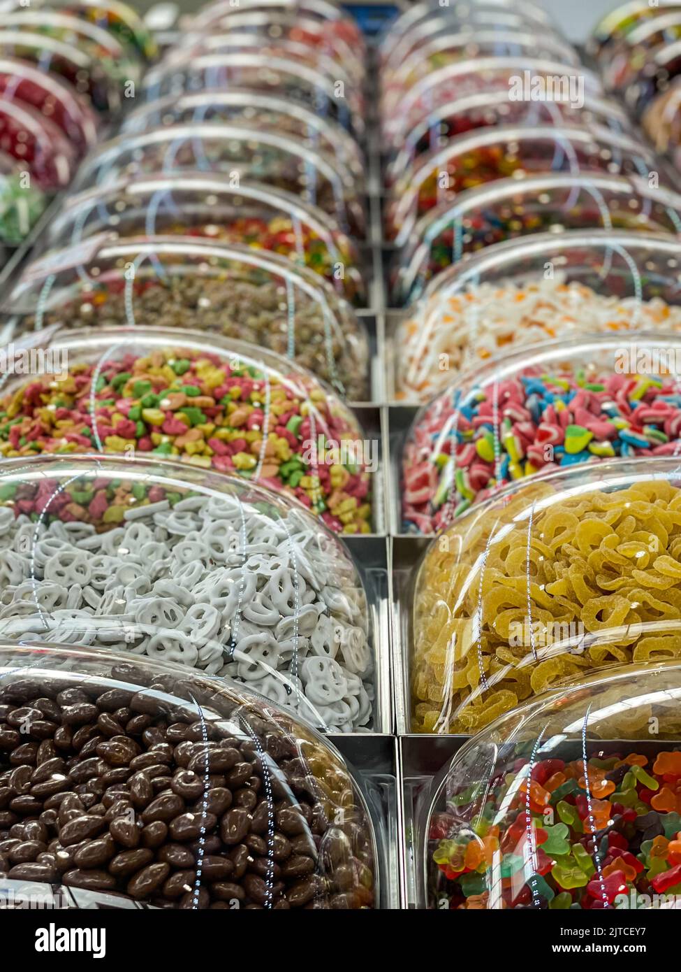 Filas de coloridos dulces azucarados se exhiben en contenedores de plástico en el quiosco de comida del centro comercial. Foto de stock