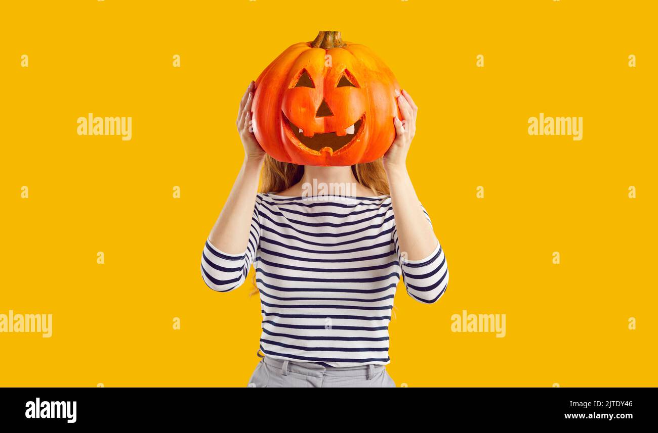 Retrato de una niña divertida con una cabeza de calabaza de Halloween sobre un fondo amarillo Foto de stock