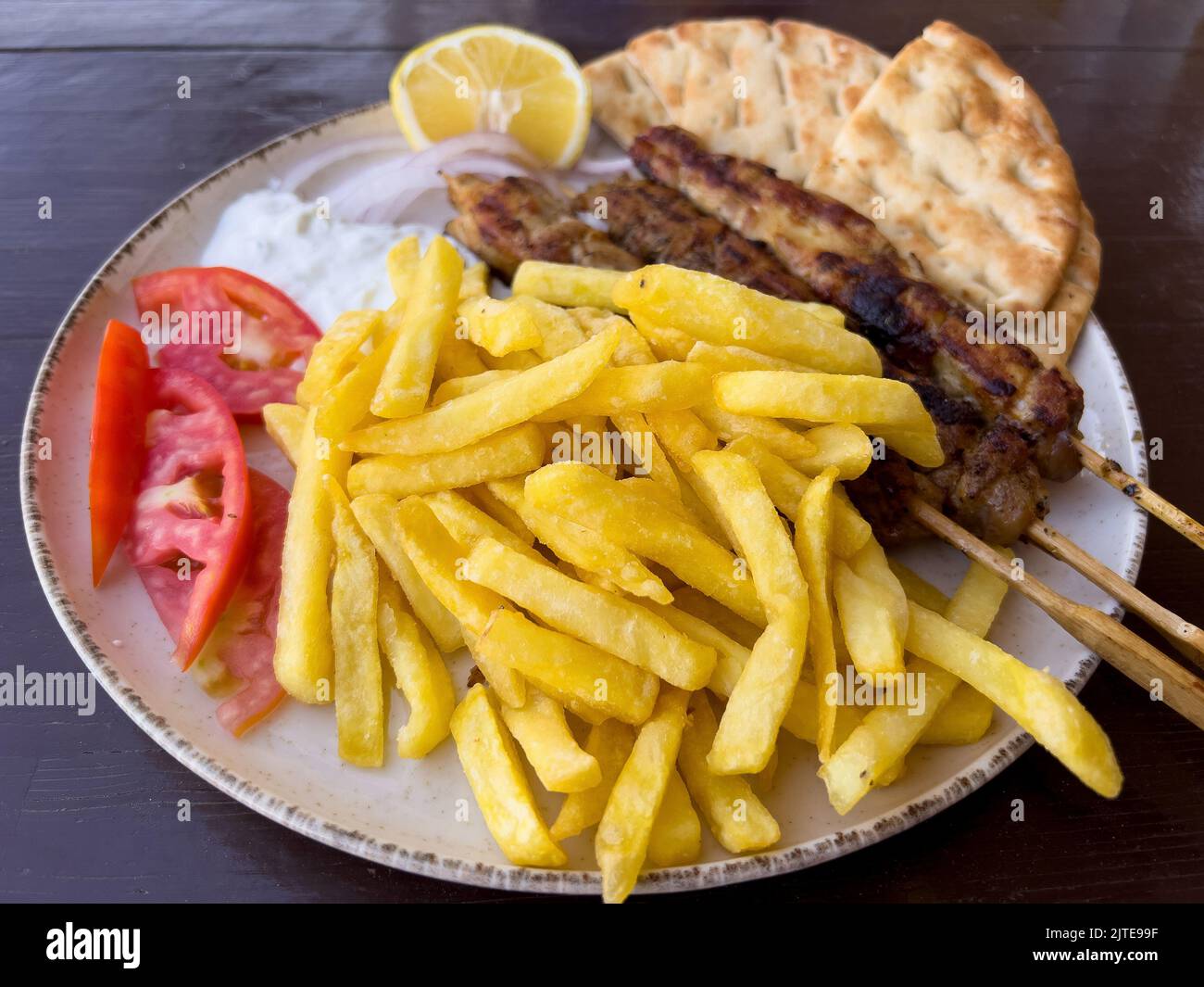 Brochetas griegas de souvlaki servidas con papas fritas, tomate, salsa tzatziki y pan de pita Foto de stock