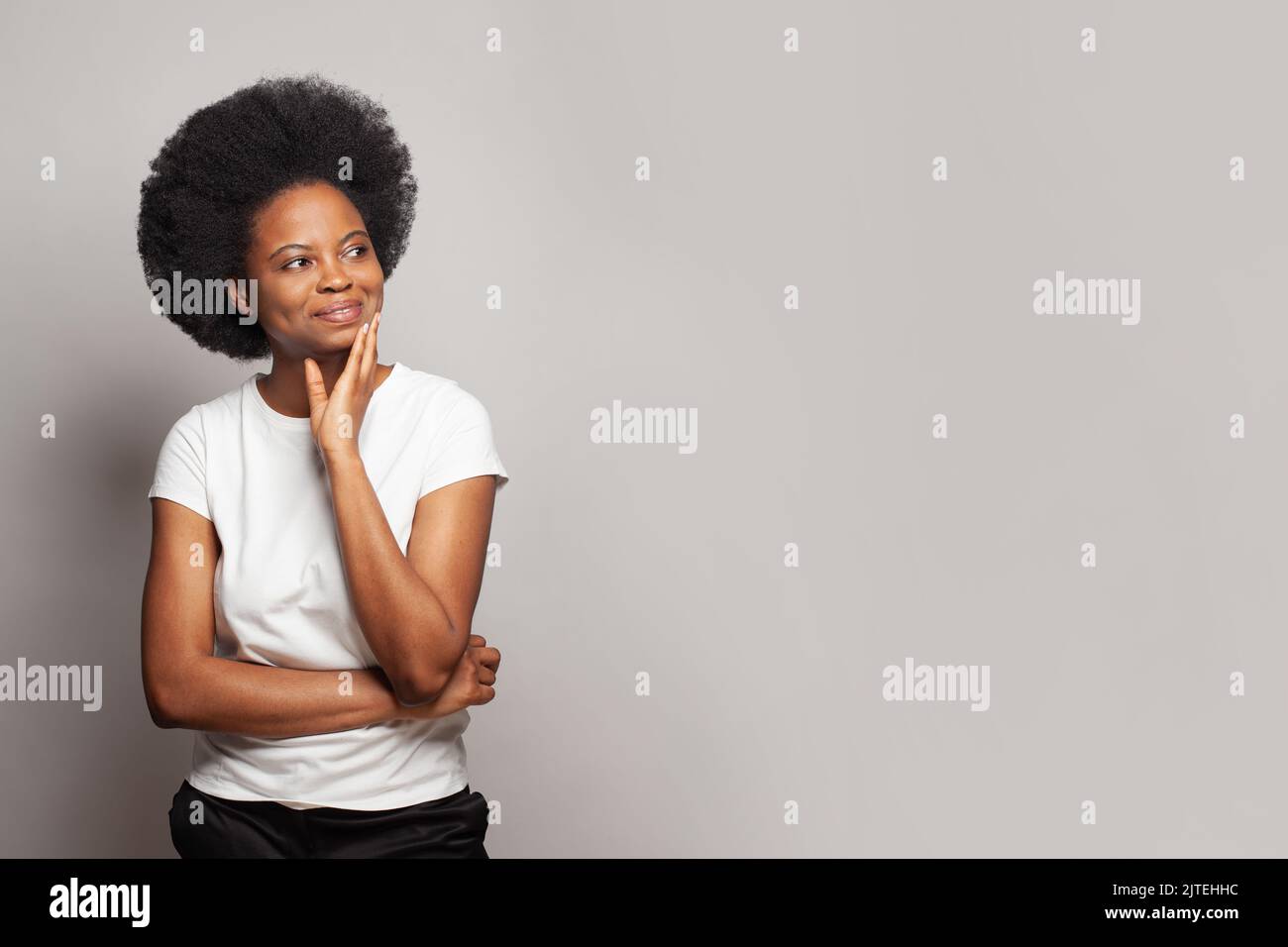Mujer joven con camiseta blanca informal sonriendo mirando el espacio de copia contra fondo blanco de la pancarta de la pared del estudio Foto de stock