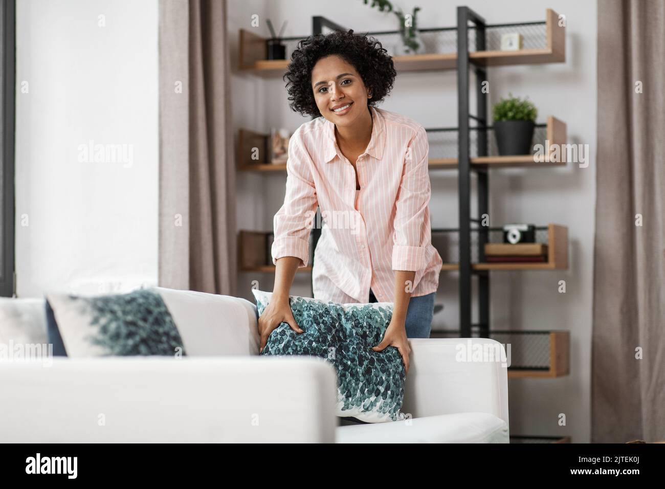 mujer feliz arreglando cojines en el sofá en casa Foto de stock