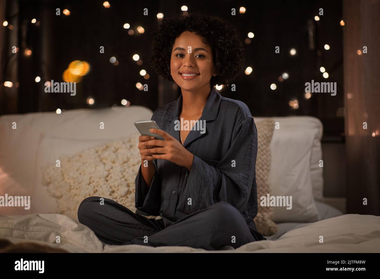 mujer feliz en pijama con teléfono en la cama por la noche Foto de stock