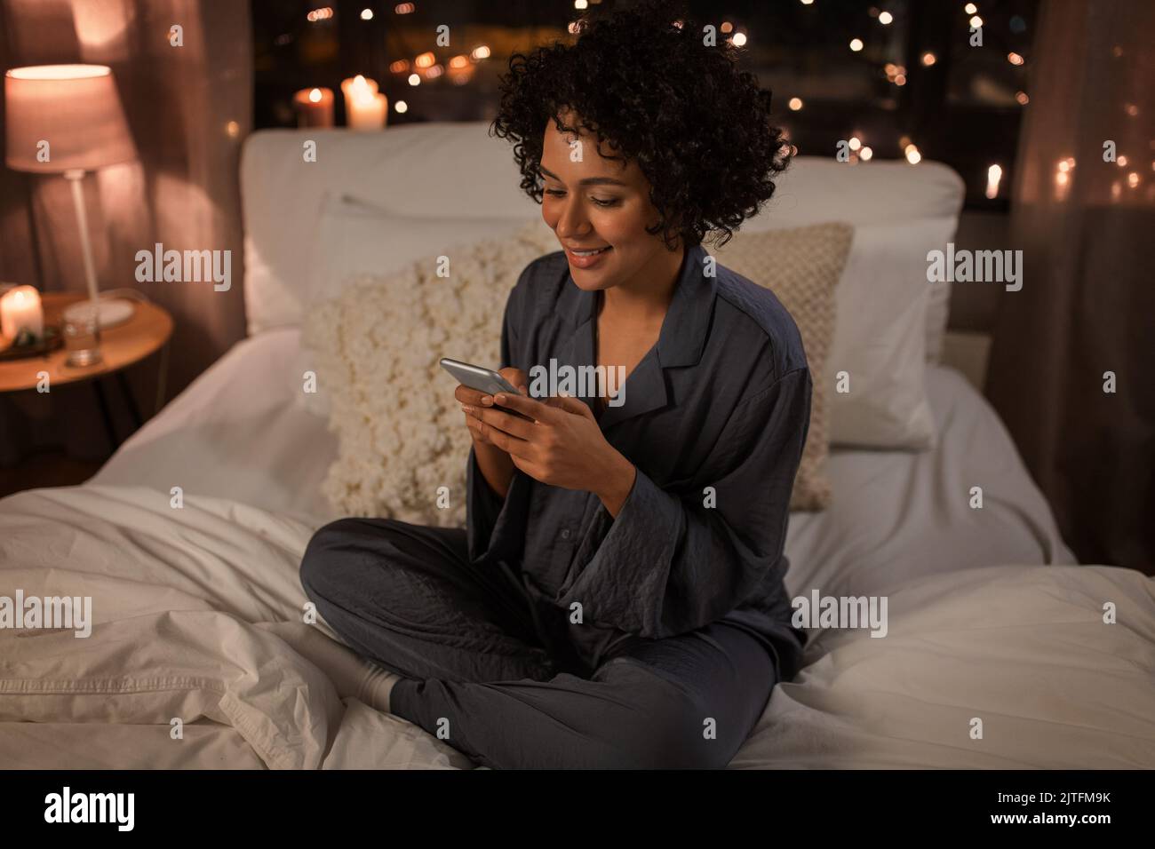 mujer feliz en pijama con teléfono en la cama por la noche Foto de stock