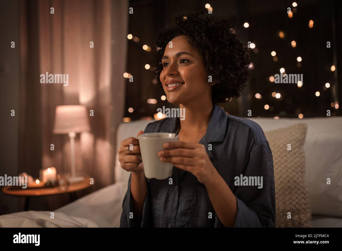 mujer feliz con café sentado en la cama por la noche Foto de stock