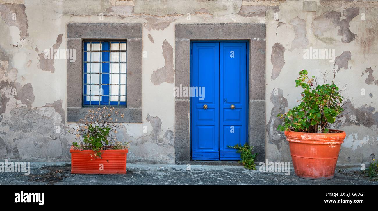 Fachada con puerta y ventana azul, con macetas en el frente. Foto de stock