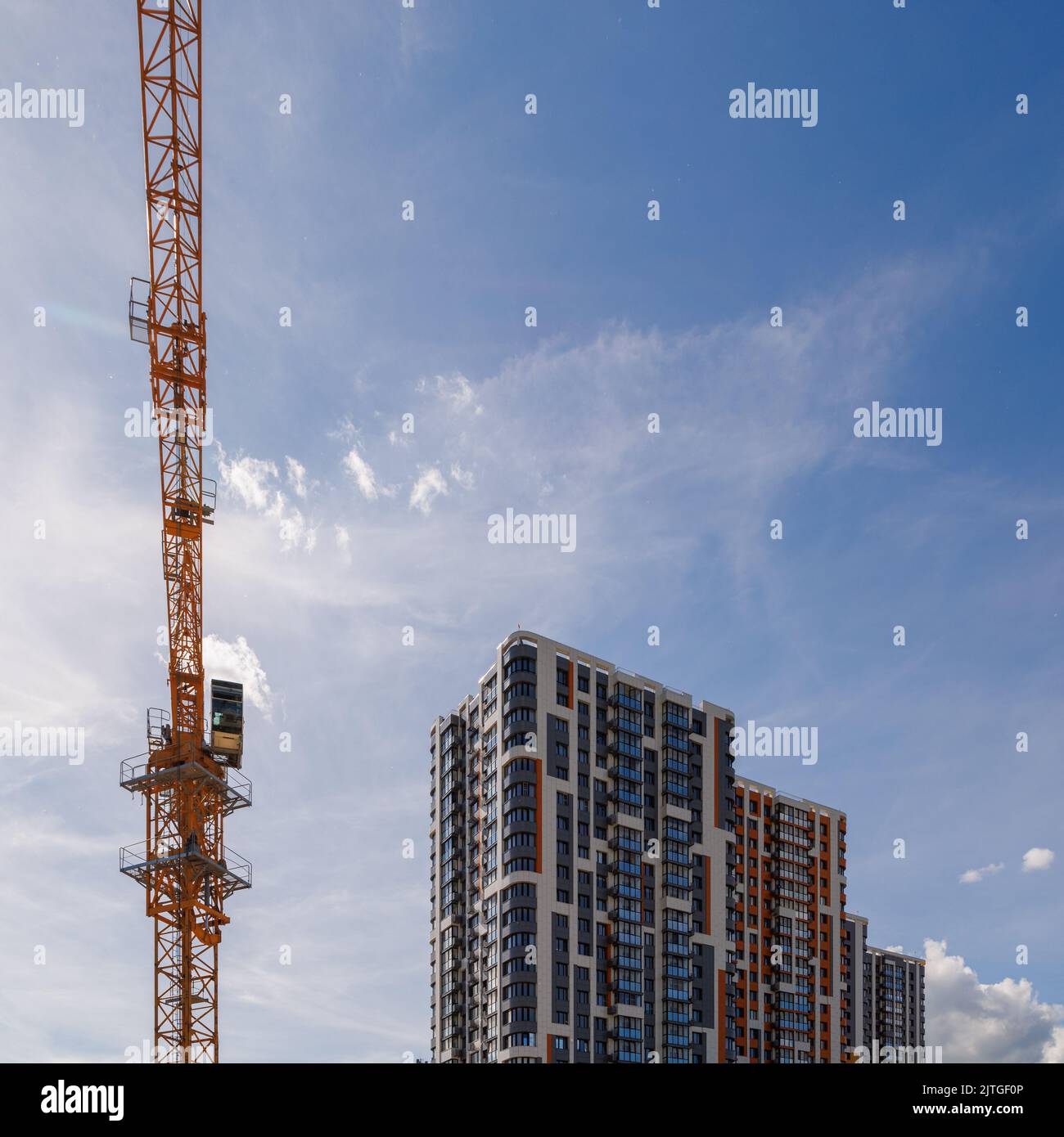 edificio de apartamentos alto recién construido cerca de la grúa amarilla sobre el fondo del cielo azul con finas nubes emplumadas Foto de stock