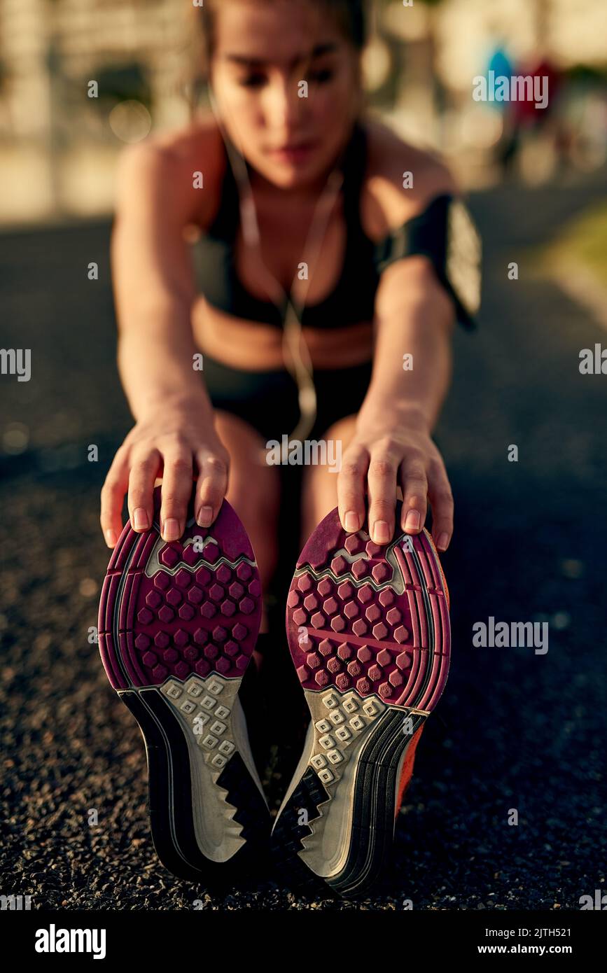 Empieza tu entrenamiento con un buen estiramiento. Una mujer joven y deportiva corriendo al aire libre. Foto de stock